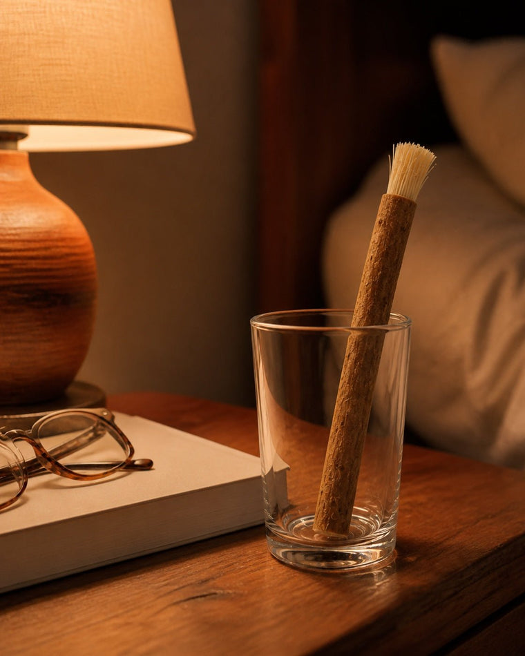 A nightstand with a lamp, reading glasses and a miswak stick standing in a glass